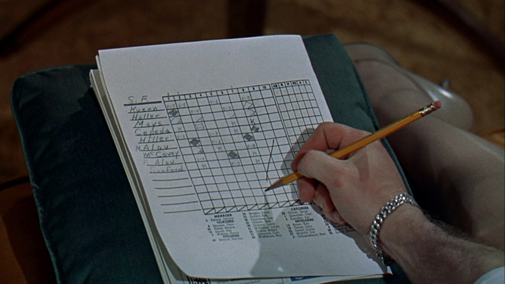 A person writing on a graph paper with a pencil, detailing names and categories in a grid format, visible on a couch.