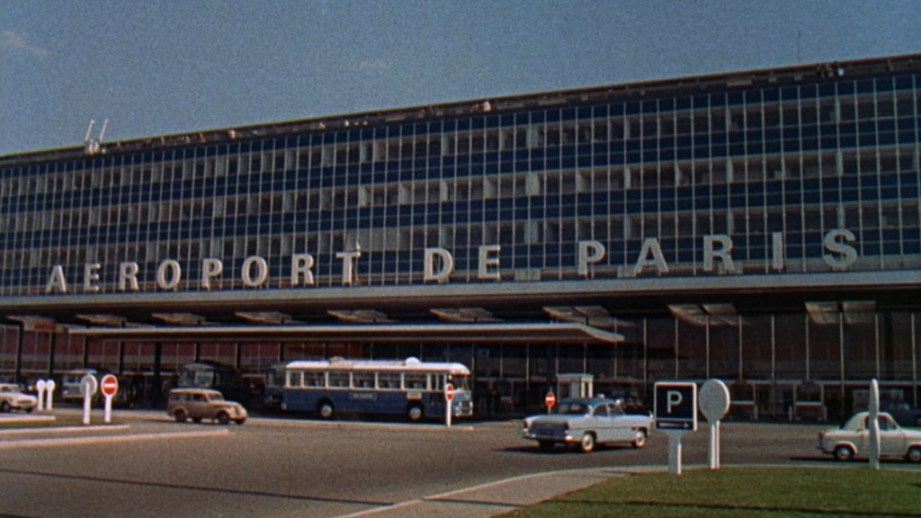Exterior view of an airport building labeled 'AEROPORT DE PARIS', featuring large glass windows and various vehicles parked out front.