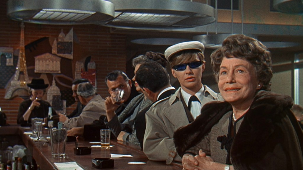 A vintage bar scene featuring a diverse group of patrons. A woman in a fur coat smiles at the camera, while a young person in stylish sunglasses and a hat stands nearby. Other patrons can be seen at the bar, some holding drinks, with decorated walls in the background.