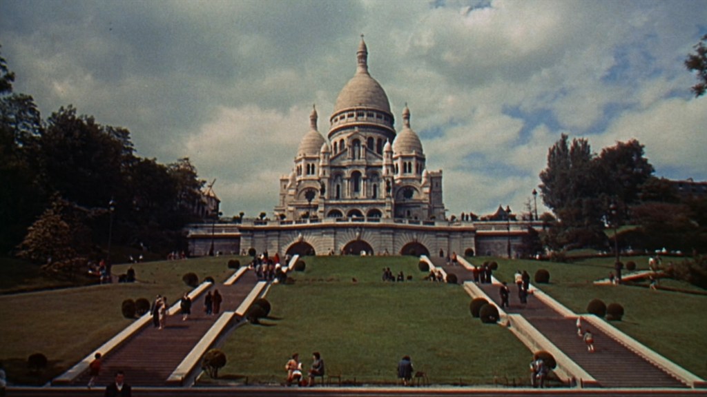 View of the Sacré-Cœur Basilica in Paris with a grassy lawn and pathways leading to the entrance, under a cloudy sky.