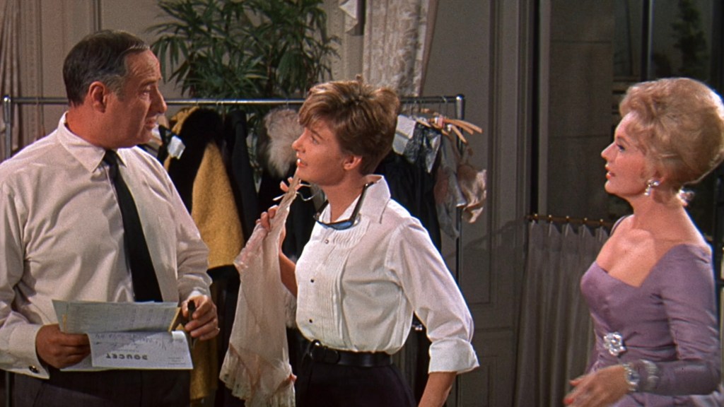 Three characters engaged in conversation in a fashion setting, with a rack of clothes in the background.