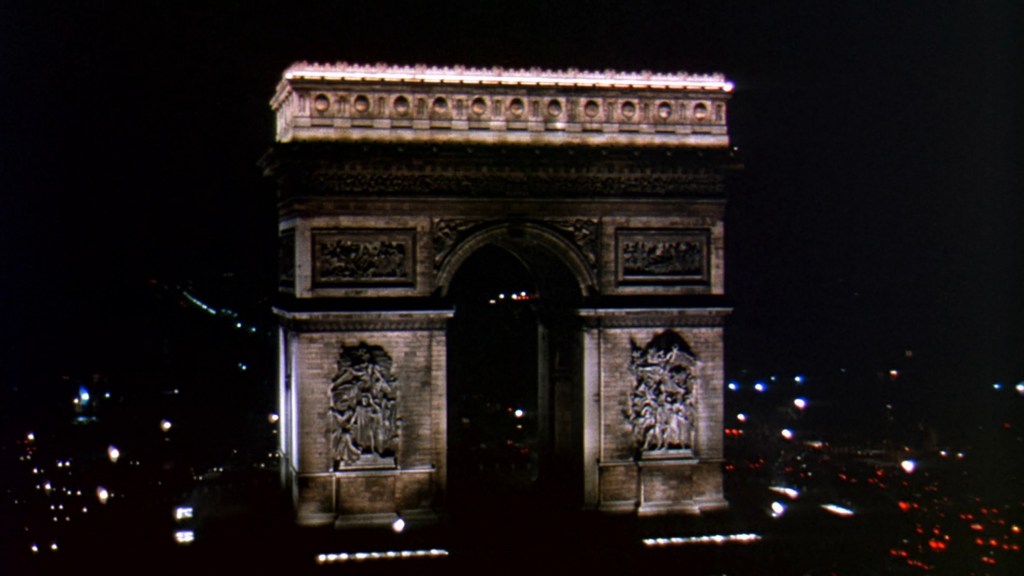 Arc de Triomphe illuminated at night in Paris, surrounded by city lights.