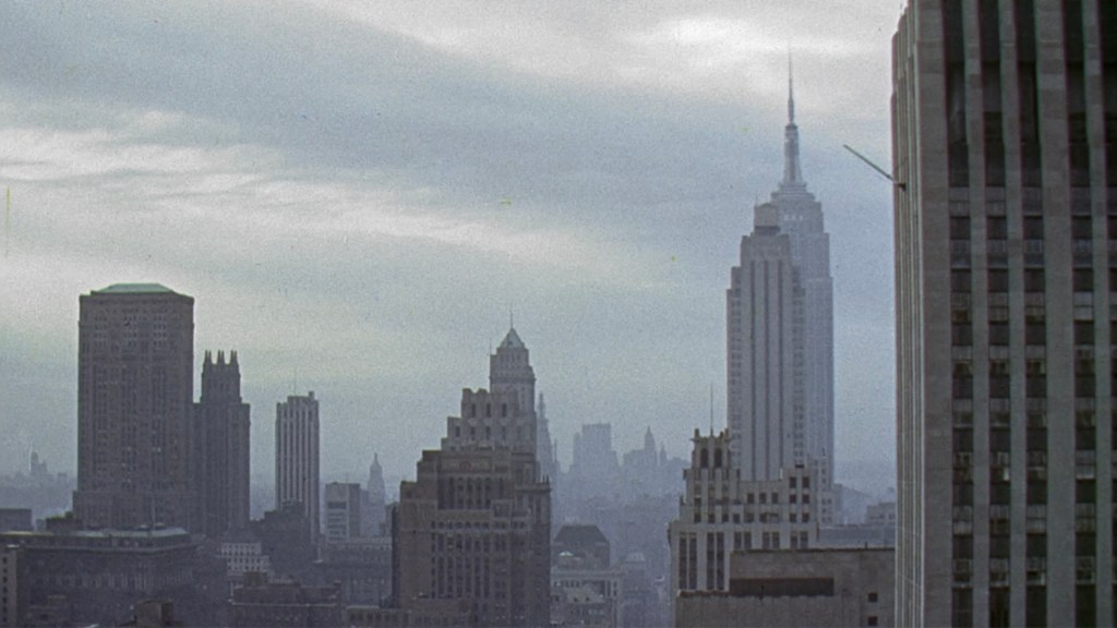 A panoramic view of a city skyline featuring various buildings, including the Empire State Building, under a cloudy sky.