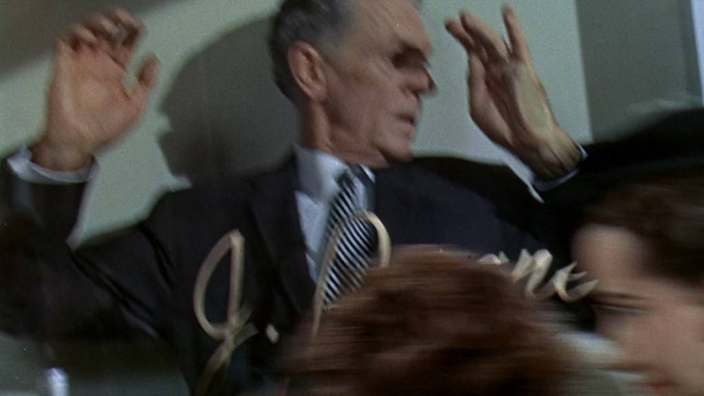 A man in a suit raises his hands in surprise or defense, while a blurred figure moves past him.