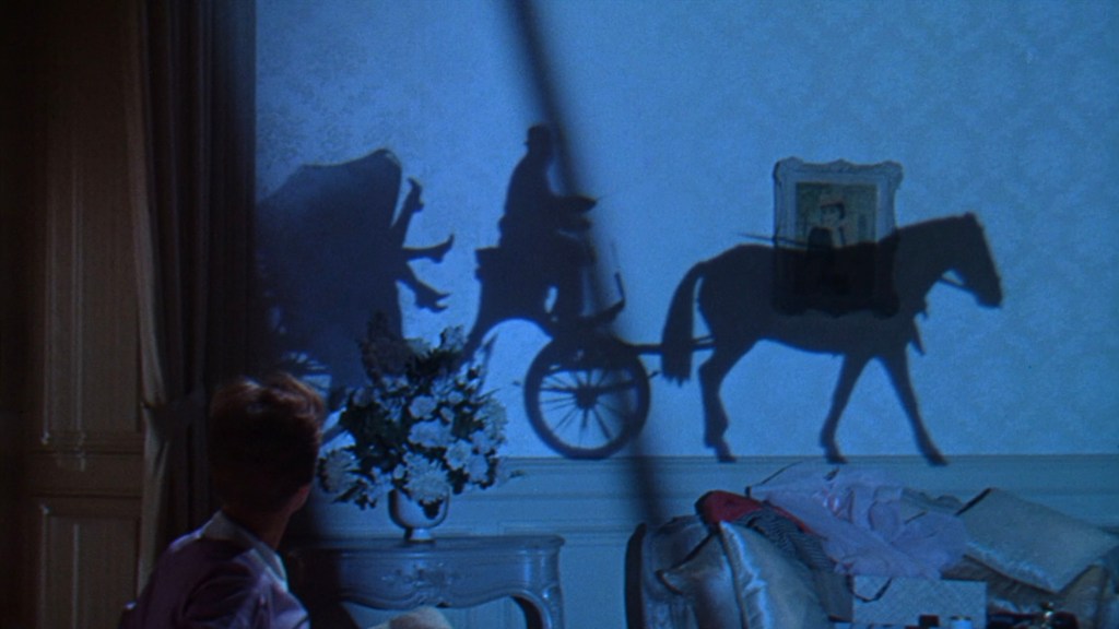 A silhouette of a horse-drawn carriage casts a shadow on a wall, while a person observes from the foreground.