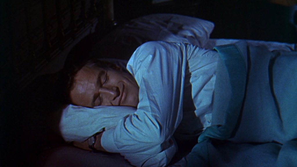 A man peacefully sleeping on a bed, smiling softly while resting his head on a pillow.