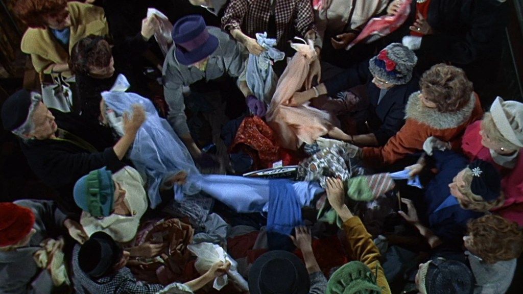 A crowded scene of women grabbing and sorting through a pile of colorful clothing, showcasing a chaotic shopping environment.