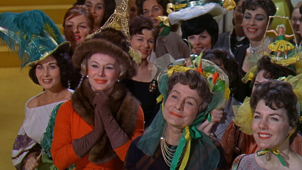 A group of women in colorful, elaborate hats, some adorned with decorative elements, smiling at an event.