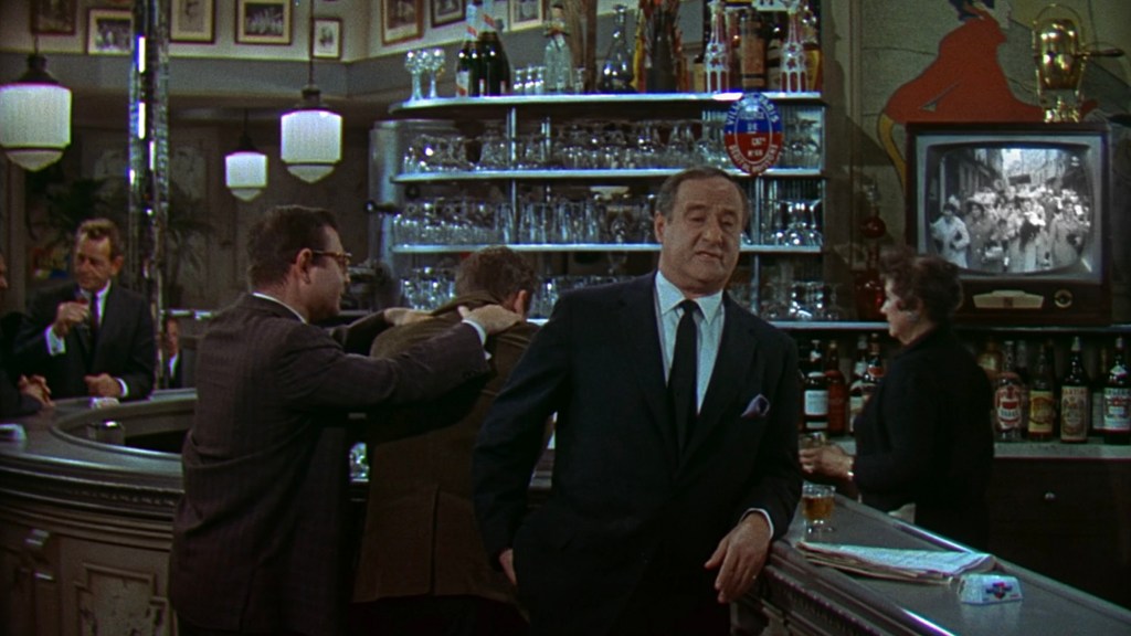 A vintage bar scene with a well-dressed man standing at the counter, surrounded by other patrons. The bar features a variety of liquor bottles and glassware, while a black and white television displays a scene in the background.
