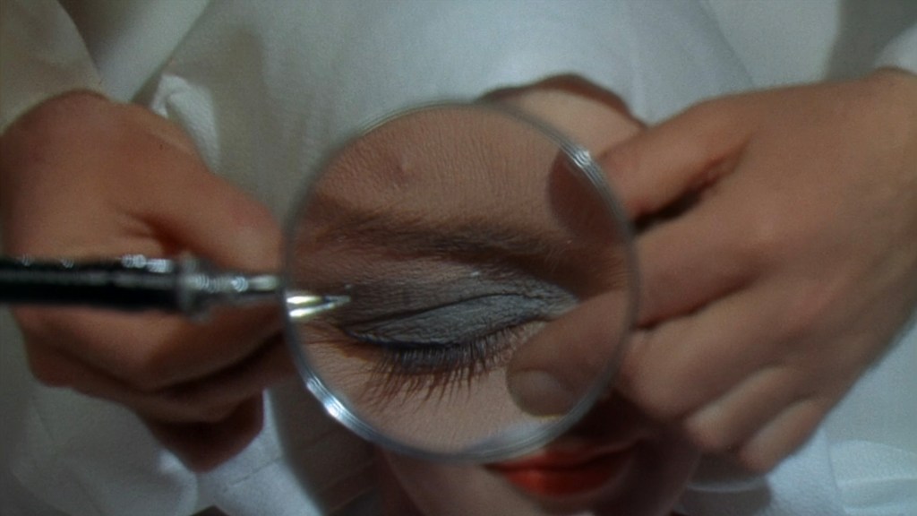 A close-up of a person applying makeup around a closed eye, with a magnifying glass bringing attention to the detailed application of eyeliner.