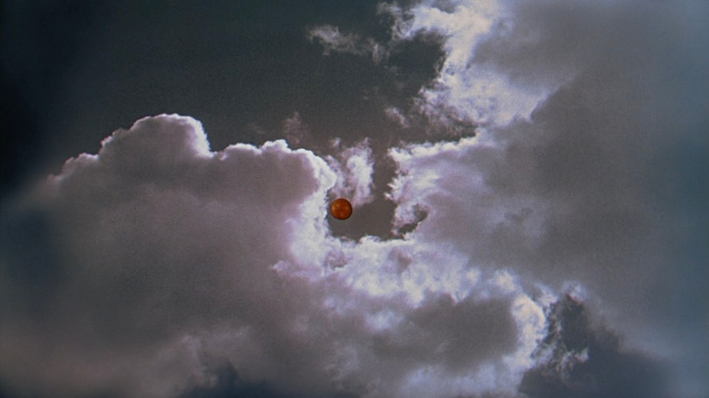 A bright orange sun peeks through dark storm clouds in a dramatic sky.