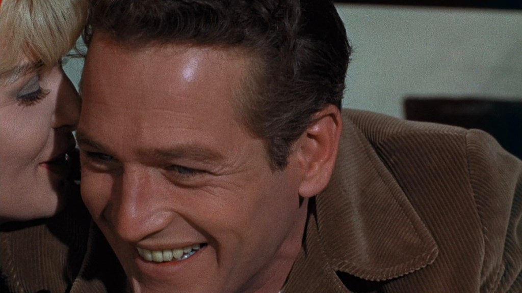 A man smiling warmly while a woman whispers in his ear, creating an intimate atmosphere.