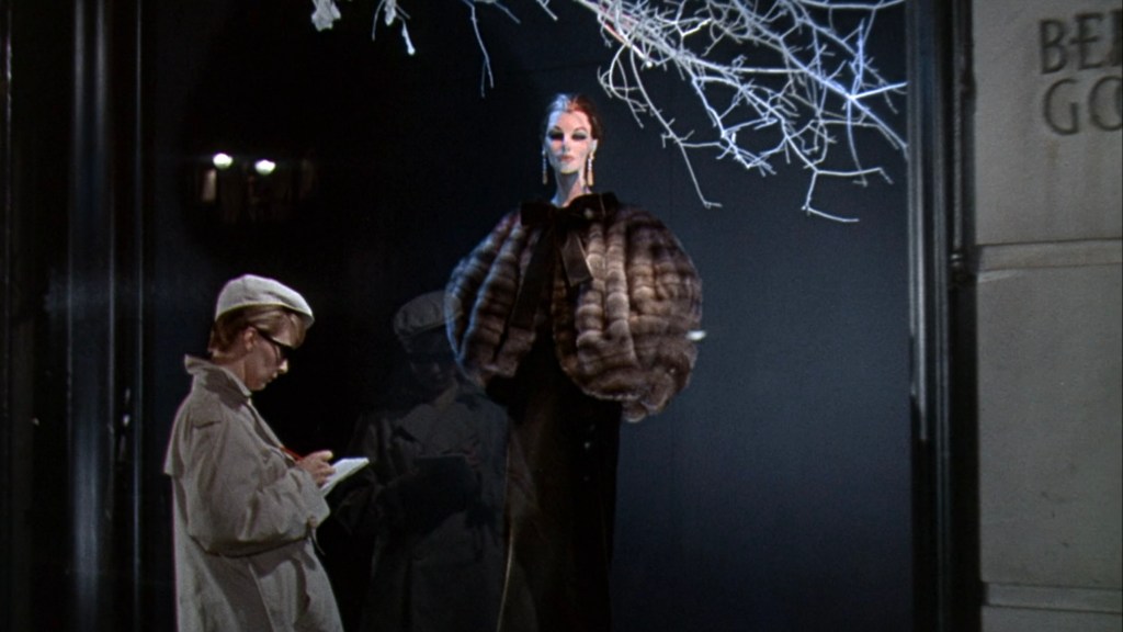 A mannequin dressed in a luxurious fur coat stands in a window display, while a child in a white cap takes notes nearby.