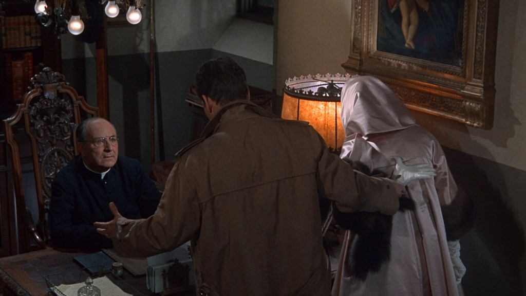 A tense scene featuring a man in a brown coat conversing with a seated priest in a dimly lit room, while a woman in a pink outfit stands beside him.