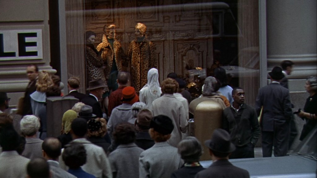 A crowd of people gathered outside a store, admiring window display mannequins dressed in leopard print coats, with some pedestrians walking by in the background.