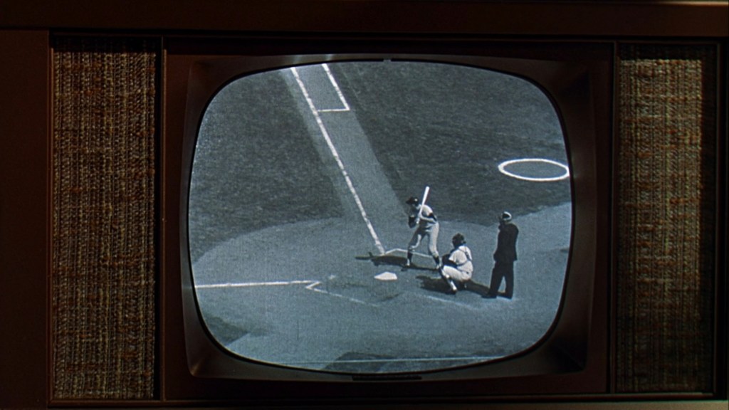 A vintage television displaying a black and white baseball game, featuring a batter preparing to hit while a catcher and umpire are positioned at home plate.