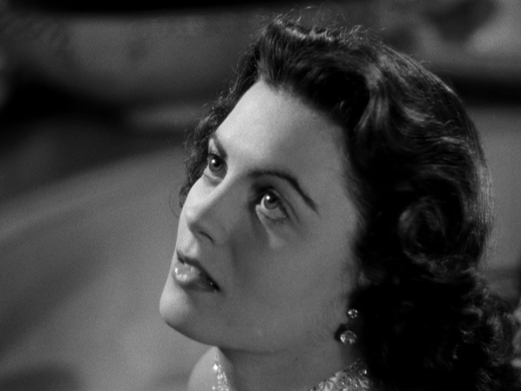 Close-up of a woman with wavy dark hair looking upwards, her expression thoughtful or reflective.