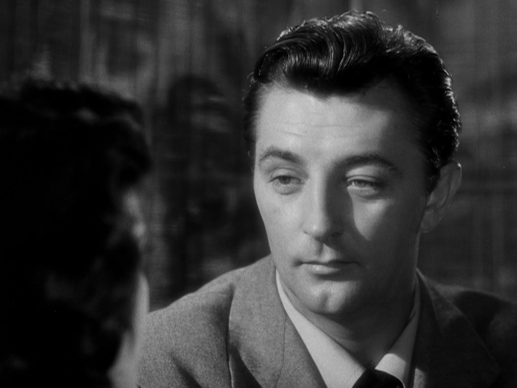 Black and white portrait of a man in a suit, looking thoughtfully to the side while engaged in conversation.