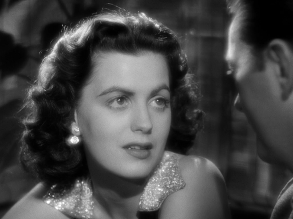 A close-up of a woman with curly hair and earrings, gazing intently at a man off-screen, set in a black-and-white film style.