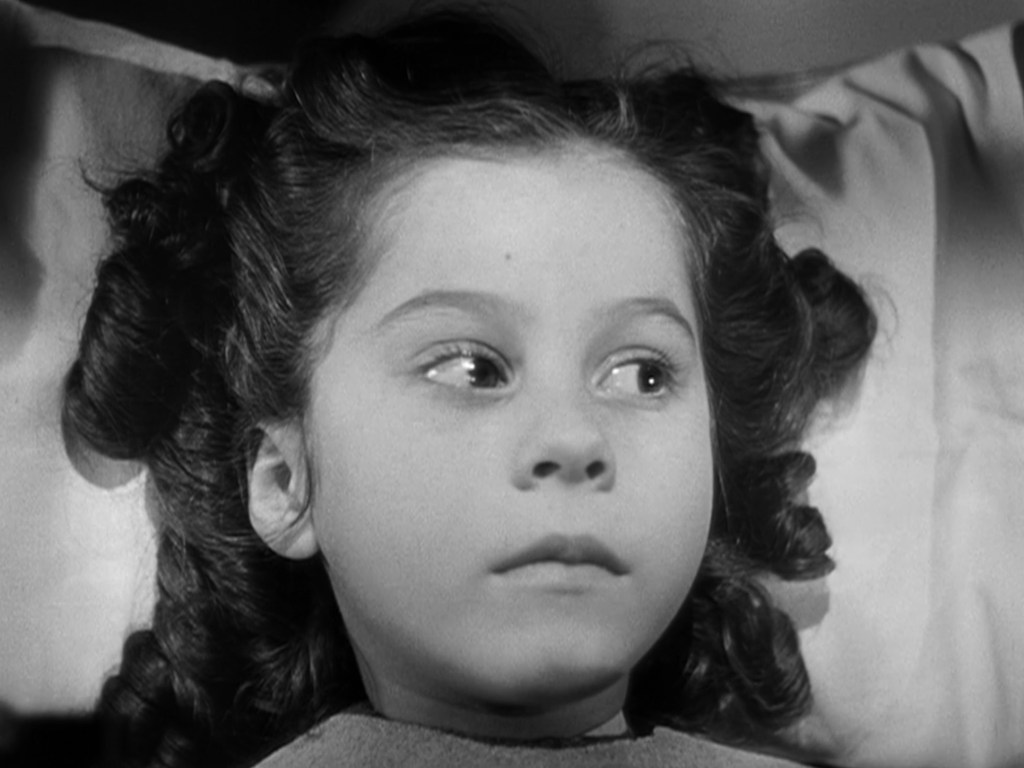 A close-up image of a young girl with curly hair lying on a pillow, looking thoughtfully to the side.