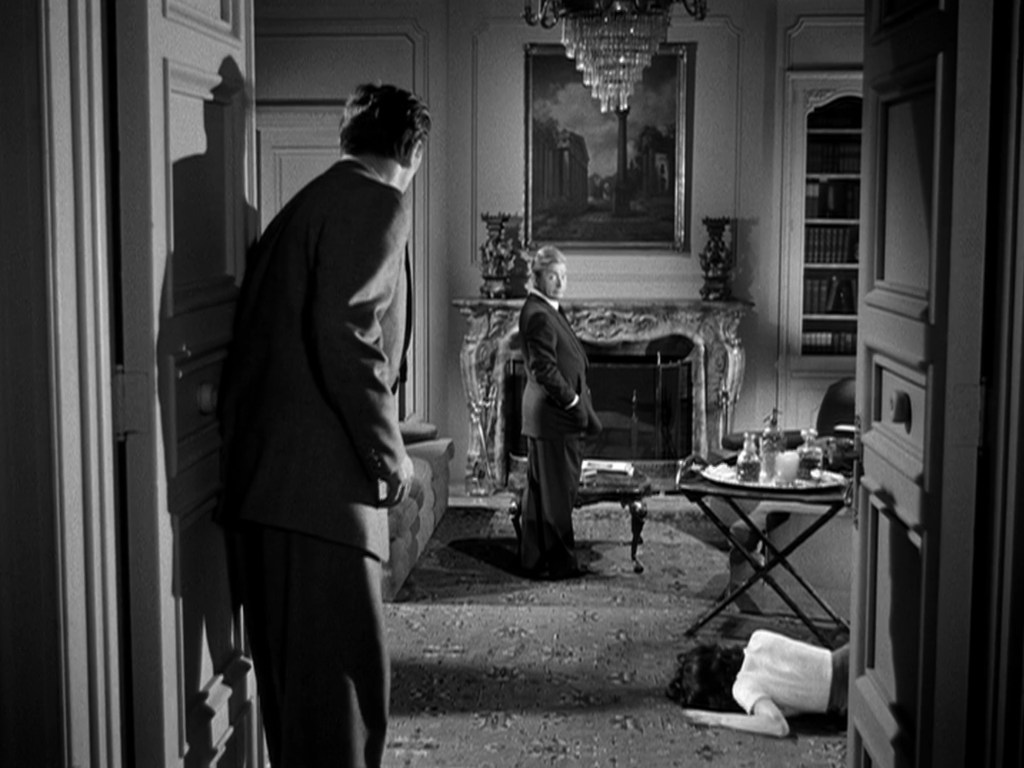 A tense interior scene with two men in formal attire. One man stands facing a fireplace adorned with a painting, while the other appears to be peering from a doorway. A woman lies on the floor in the foreground.