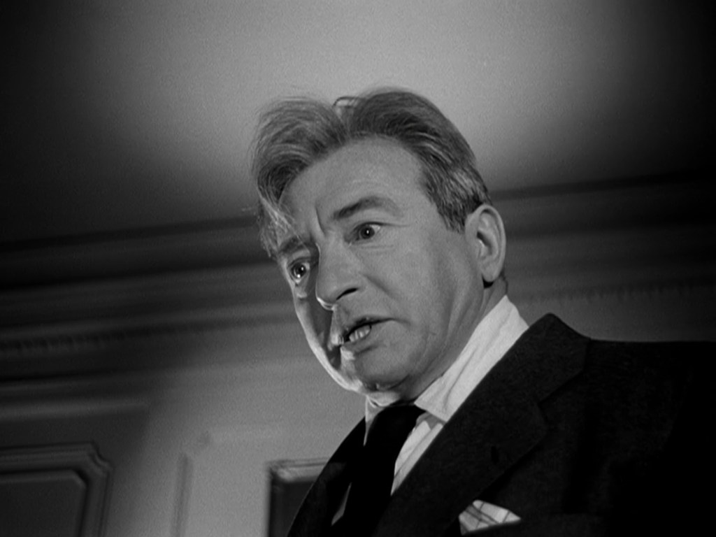 A close-up of a man in a suit with an intense expression, looking upward with a concerned or angry demeanor.