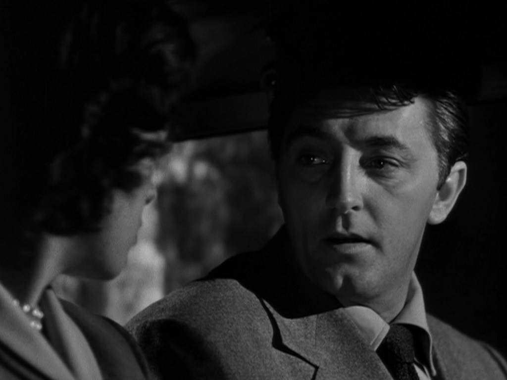 A close-up of two characters in a car, one man looking intently at a woman, with dramatic lighting creating a somber atmosphere.
