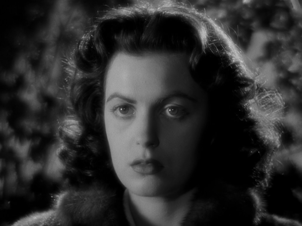 A close-up of a woman with curly hair and a serious expression, captured in black and white.