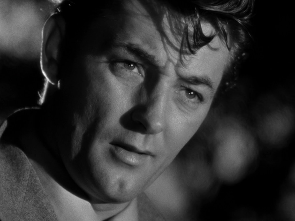 Close-up of a man with short, wavy hair, gazing thoughtfully in black and white.