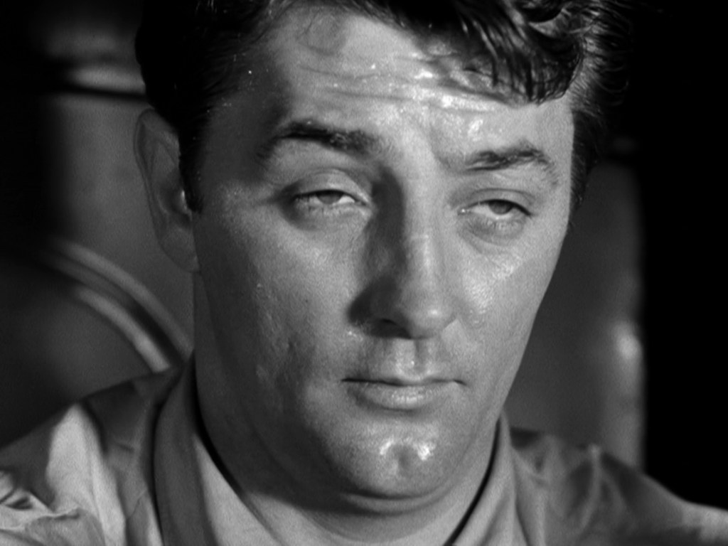 A close-up of a man with slicked-back hair and a weary expression, appearing deep in thought or troubled, captured in black and white.