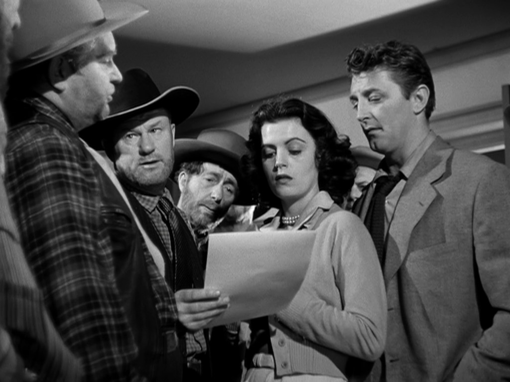 A group of characters, including a woman in a cardigan and several men in hats and plaid shirts, gathered around a piece of paper, looking concerned and engaged.