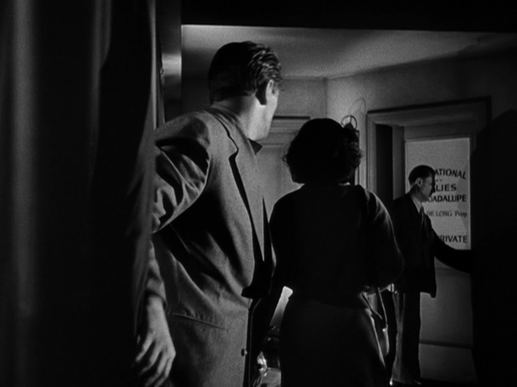 A group of three people entering a dimly lit corridor, facing a door with a sign that reads 'NATIONAL LIES GUADALUPE' and 'PRIVATE.' The scene is in black and white, emphasizing the shadows and mysterious atmosphere.