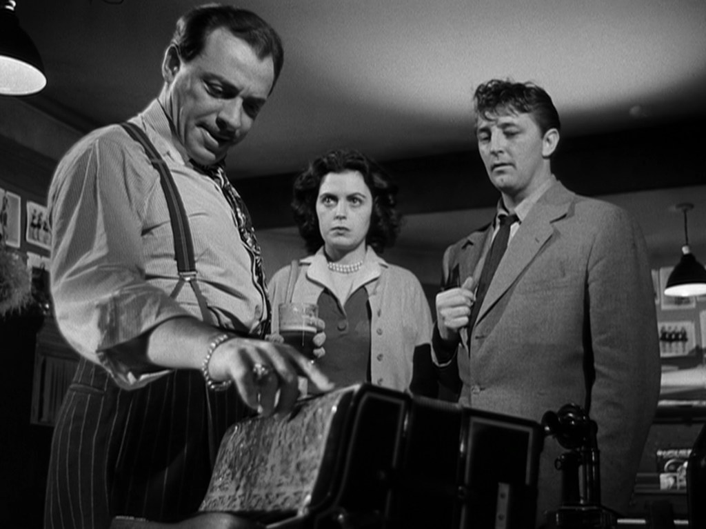 A tense scene in a vintage bar where three characters are engaged in a serious discussion, with one man examining a cash register while a woman and another man look on with concern.