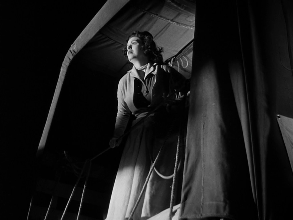 A woman standing on a platform, looking thoughtfully into the distance, framed in shadows, with a dark and moody atmosphere.