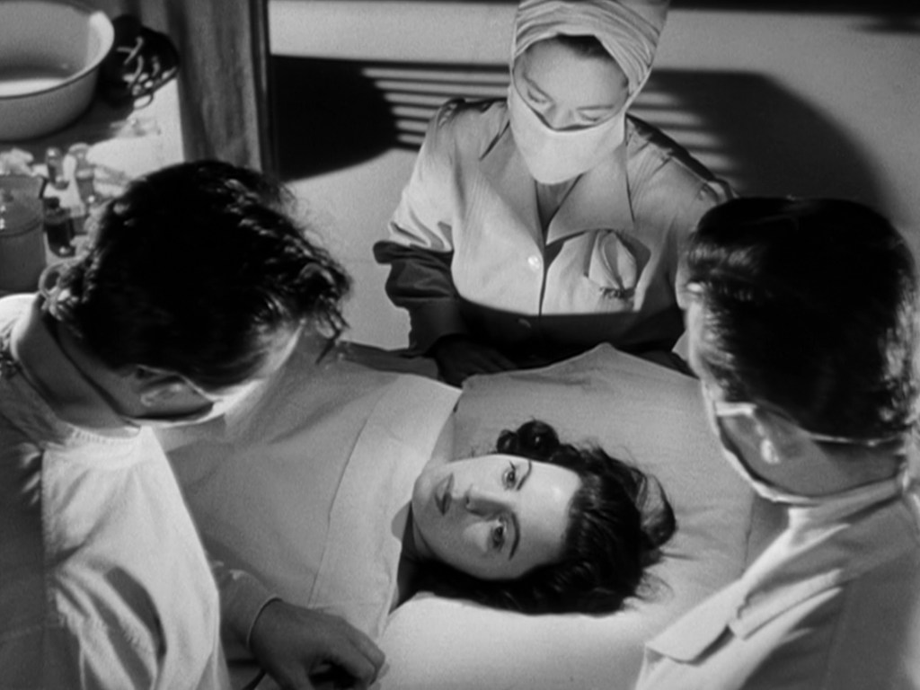 Medical scene depicting a patient lying on an examination table while three medical professionals, including a nurse, are attending to her in a dimly lit room.
