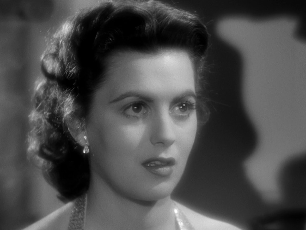 Close-up portrait of a woman with styled dark hair and earrings, looking thoughtfully with a serious expression.