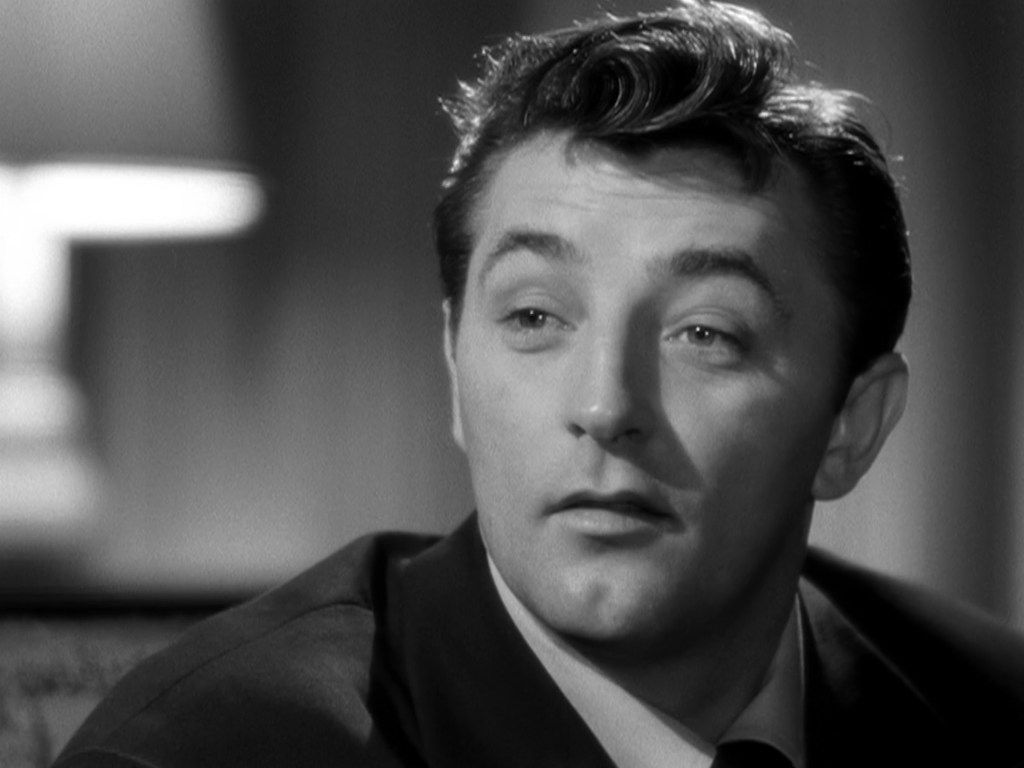 Close-up of a man with dark hair and a suit, looking thoughtfully to the side in a black and white setting.