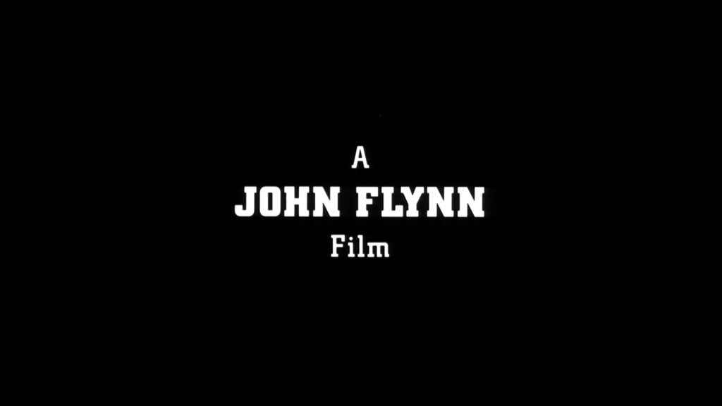 Title screen for a film, featuring the phrase 'A JOHN FLYNN Film' on a black background.