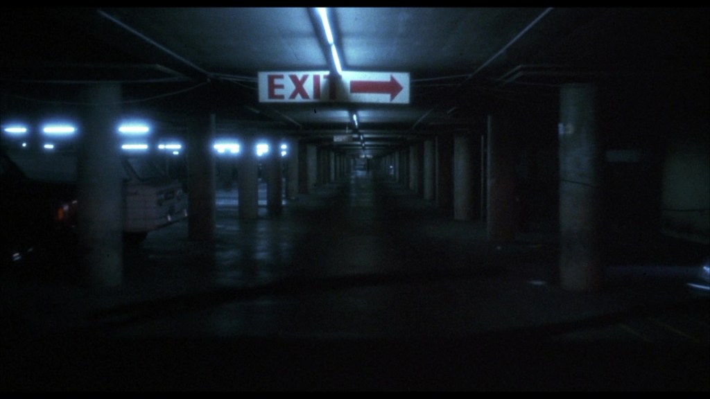 Dimly lit underground parking garage with concrete pillars and an illuminated EXIT sign pointing right.