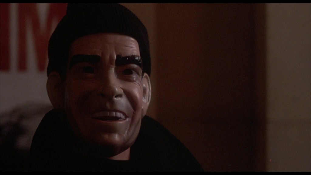 Close-up of a creepy mask with exaggerated facial features, wearing a black beanie.