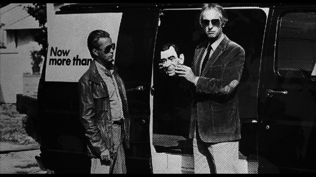 Two men standing next to a van, one holding a puppet head. The van has the text 'Now more than' visible.