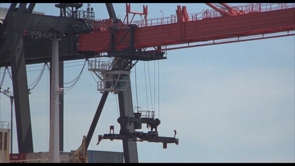Close-up view of a large industrial crane with a suspended load, set against a blue sky.