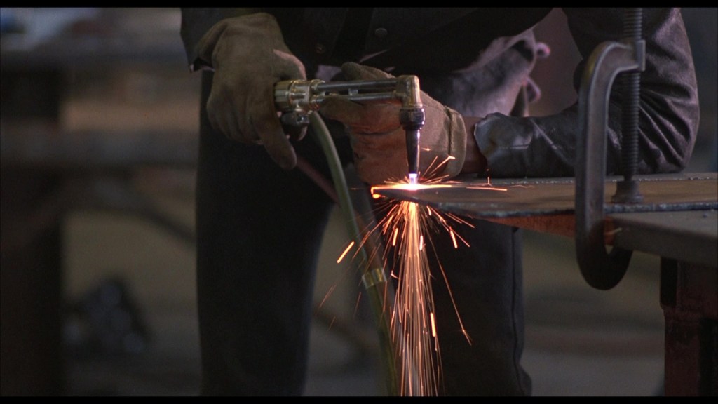 A welder using a torch to cut metal, with sparks flying from the cutting point.