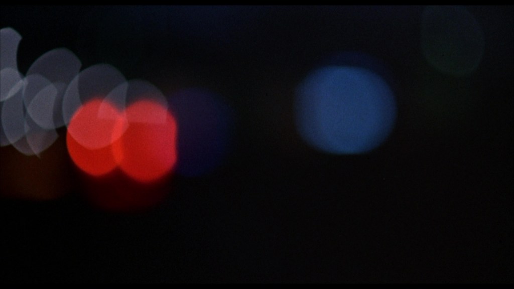 Out-of-focus lights in varying colors, predominantly red, blue, and white, against a dark background, creating a bokeh effect.