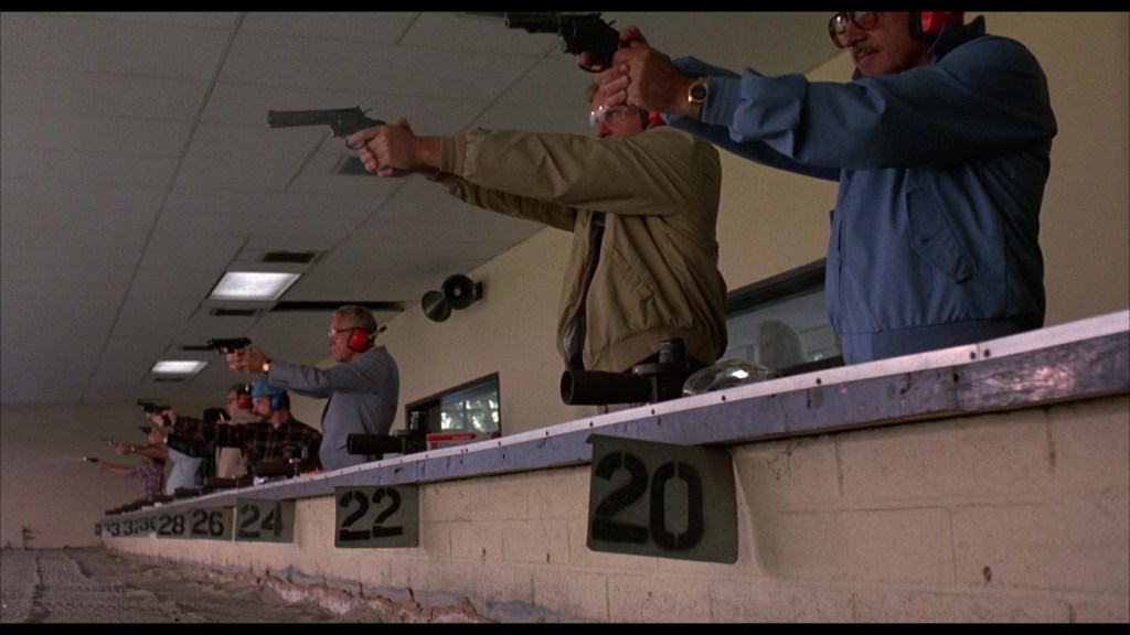 A group of individuals at a shooting range, each aiming handguns at targets, with protective ear coverings and safety gear.