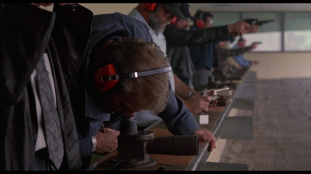 A group of people at a shooting range, focusing on their targets while holding firearms. Some individuals are adjusting their equipment, and all are wearing hearing protection.