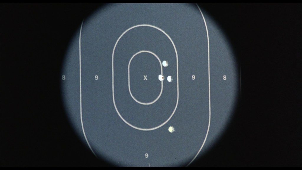 Close-up view of a shooting range target with bullet holes marked in concentric circles, centered around an 'X' mark.
