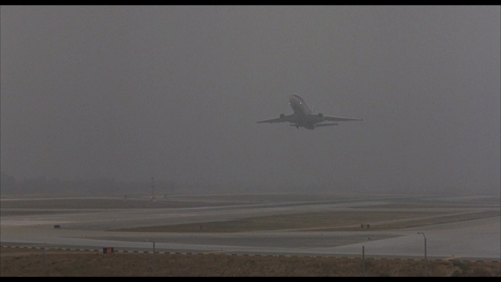 A commercial airplane takes off into a foggy sky above an airport runway.