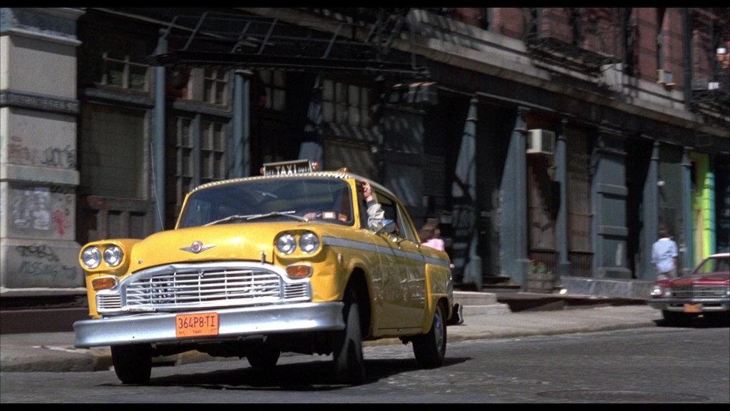 A classic yellow taxi cab driving down a city street with vintage buildings in the background.