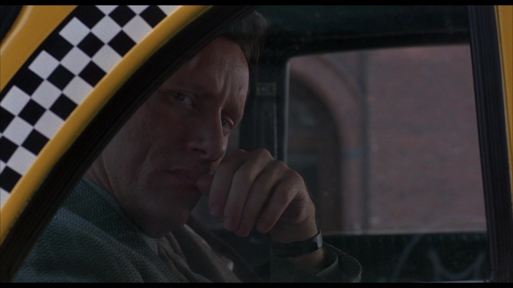 Close-up of a contemplative man in a taxi, resting his chin on his hand, with a checkered taxi window frame.